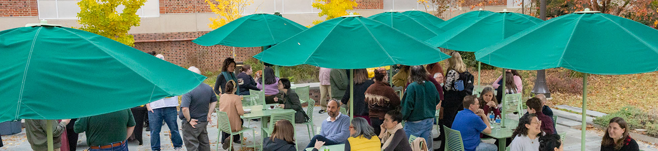 People gathered on the Swem Patio under large green patio umbrellas