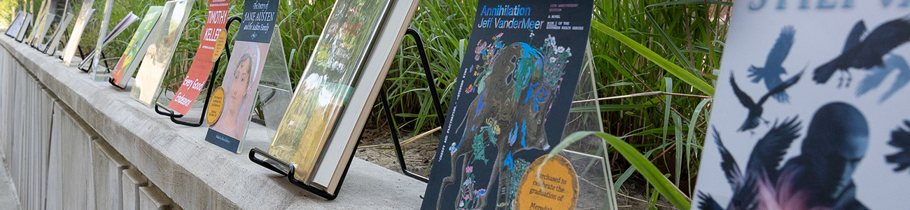 Books selected by Swem's graduating student employees are displayed along a concrete wall on the patio