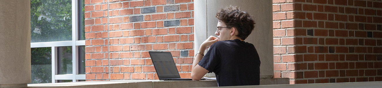 Student working on a laptop at the front entrance of Swem