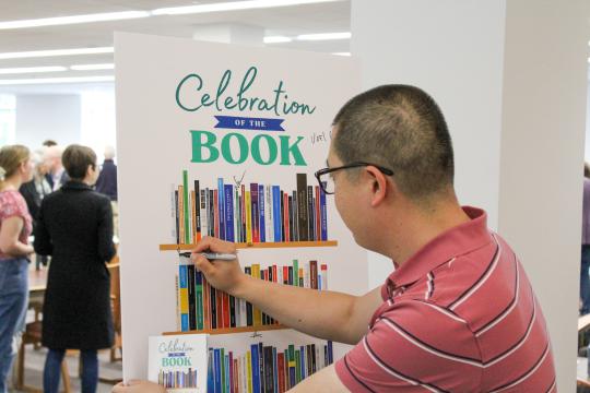 Faculty member signs their name to a poster for Celebration of the Book