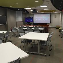 Ford Classroom with projection screen and furniture arranged in tables seating 4 each