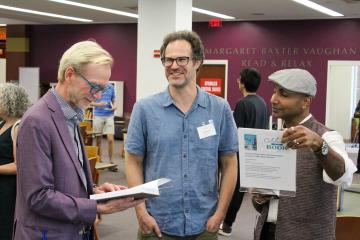 Three people gathered together in Read & Relax looking at a faculty book recently published