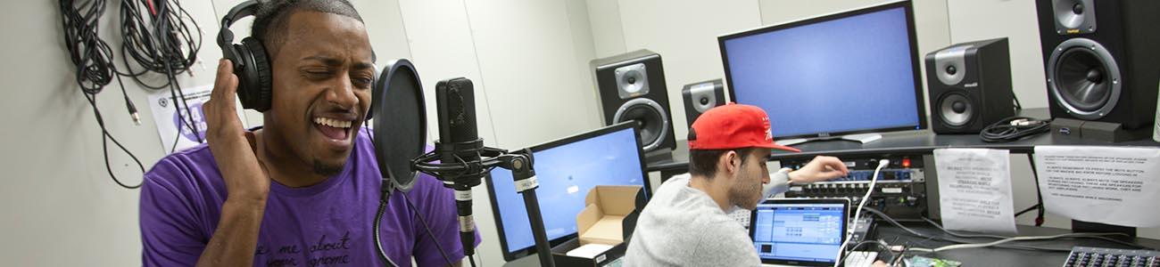 Two students in a media center studio - one student at a computer and the other sings into a microphone