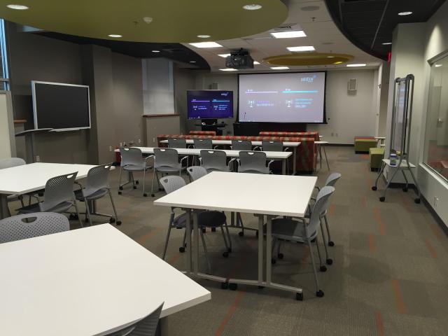 Ford Classroom with projection screen and furniture arranged in tables seating 4 each