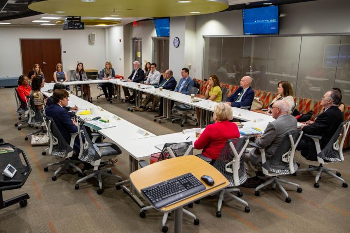 Large group seated in the Ford Classroom around desks arranged in the shape of a rectangle