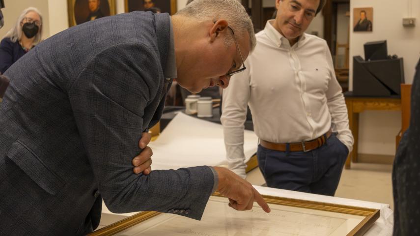 Two people examine the framed diploma up close.