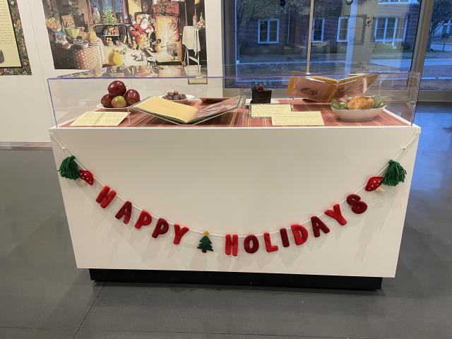 Exhibit case with felt banner reading Happy Holidays with books and food items inside