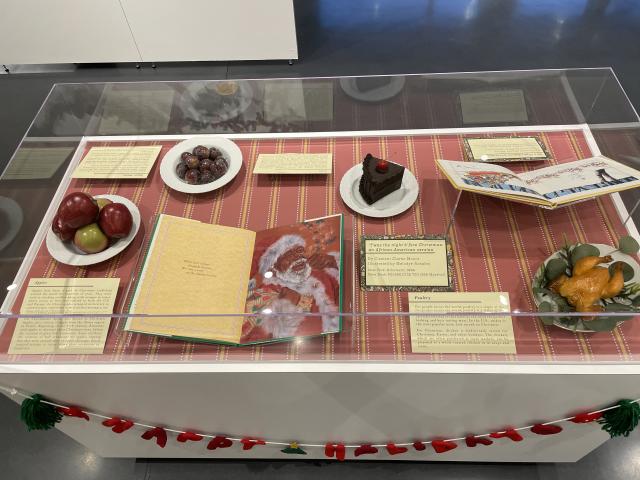 Exhibit case with food, books, and labels about holiday food culture in 'Twas the Night Before Christmas