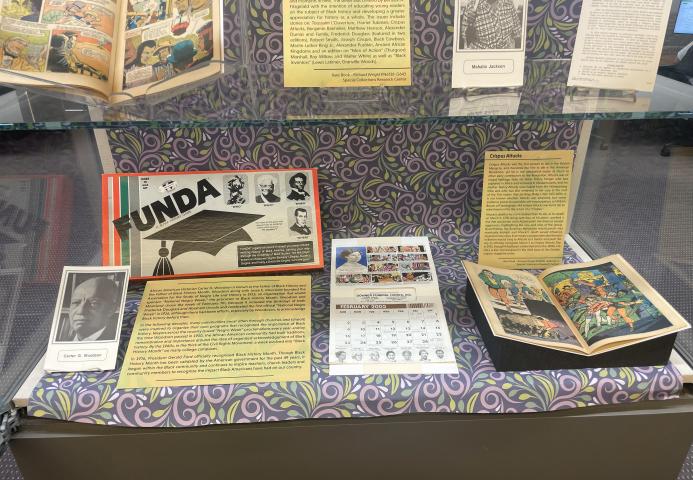 Exhibit case with Black History educational items such as board games, calendars, and comic books.