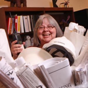 Kay Domine holding a walkie talkie and surrounded with hard hats and building plans