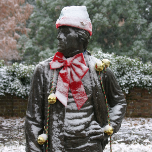 Snow covered statue on campus decorated with holiday bows and cap