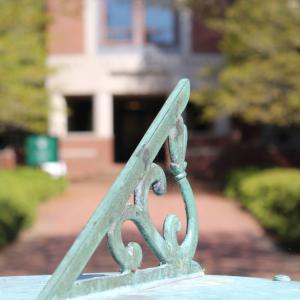 Closeup of the arm of a sundial with Swem in the background