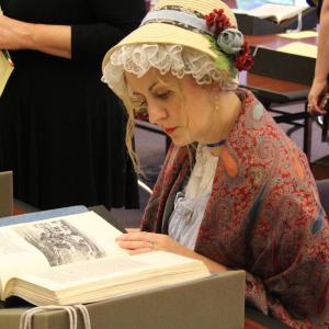 A person dressed in Jane Austen period attire examines a book in Special Collections