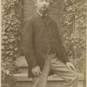 Portrait of Charles Swinburne in front of brick wall covered in ivy