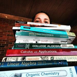 Person holding a large stack of textbooks