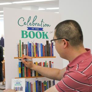 Faculty member signs their name to a poster for Celebration of the Book